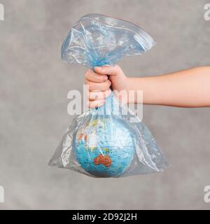 Kind Hand hält Erdkugel in durchsichtiger Plastiktüte über Grauer Hintergrund Stockfoto