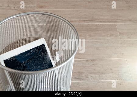 Modernes Tablet mit stark gebrochenem Bildschirm im Abfalleimer. Stockfoto