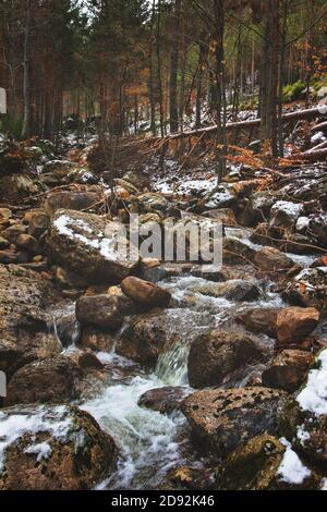 Wasser fällt zwischen den Felsen im verschneiten Fluss Stockfoto