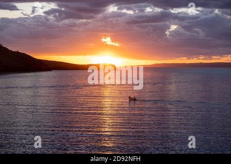 Kea, Insel Tzia, Reiseziel Griechenland. Sonnenuntergang, Sonnenaufgang orange durch Wolken über dem Mittelmeer. Die Sonne spiegelt sich auf dem Wasser, das Schnellboot segelt Stockfoto