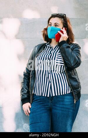 Frau mit Gesichtsmaske spricht am Telefon während Die Straße runter