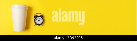 Einfach minimalistisches Design Papier Kaffeetasse und Wecker auf gelb bunten Hintergrund. Getränke zum Mitnehmen und Frühstücksgetränk. Good Morning Wake Up Wake-Konzept. Flach Lay Draufsicht Copy Space Banner Stockfoto