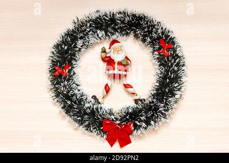 Weihnachtskranz mit roter Schleife auf beigem Holzhintergrund und weihnachtsmann-Spielzeug in der Mitte. Draufsicht Stockfoto