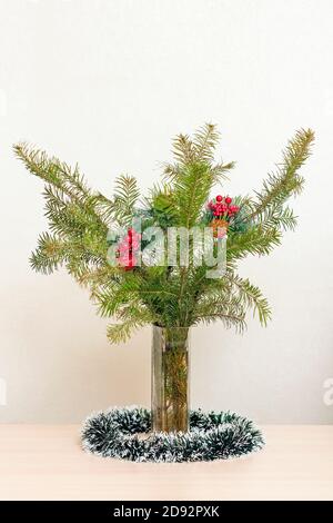 Christbaumzweige mit roten Verzierungen mit Kugeln in einer Vase auf beigem Hintergrund. Vertikale Ansicht Stockfoto