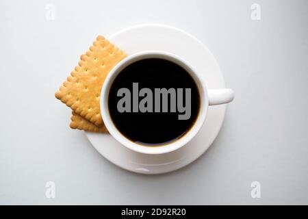 Tasse Kaffee mit Crackern auf Untertasse auf weißem Hintergrund, Draufsicht Stockfoto