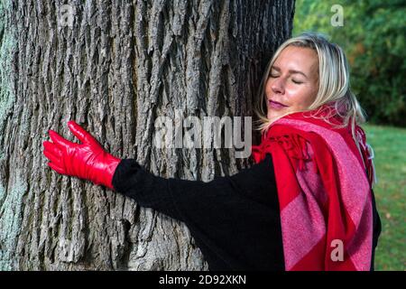 Blonde Frau in ihren 40er Jahren umarmt einen Baum im Herbst Stockfoto