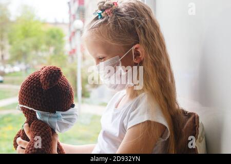 COVID-19 Coronavirus Konzept, kleines Mädchen im Gesicht medizinische Maske Blick auf Spielzeug Stockfoto