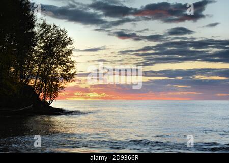 Ein brillanter Sonnenuntergang setzt Wolken über dem friedlichen Wasser in Flammen Des Lake Superior Stockfoto