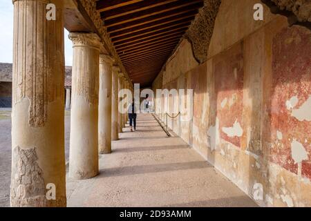 Touristen, die zwischen den Säulen vor dem Stabian Baths (Terme Stabiane) Badehaus, alten römischen Badekomplex Ruinen, Pompeji, Kampanien, Italien laufen Stockfoto