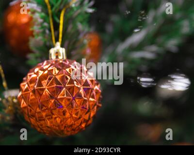 Weihnachten orange glänzende Kugel hängt auf dem grünen Zweig des Baumes. Lichter und Girlanden. Weihnachten und glückliches Neujahrskonzept, Raum für Text für Sie Stockfoto