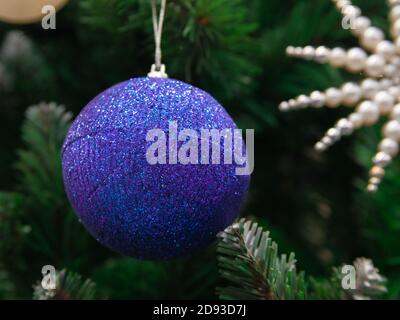Weihnachtliche dunkelblaue glänzende Kugel, die auf dem grünen Zweig des Baumes hängt. Lichter und Girlanden. Weihnachten und glückliches Neujahrskonzept, Platz für Text für Stockfoto