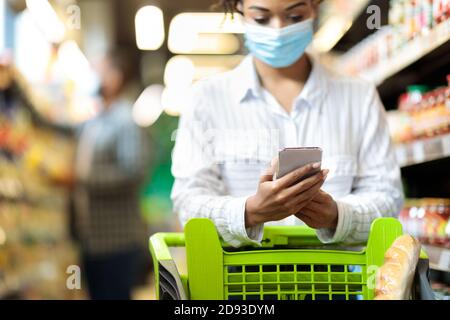 Afrikanische Frau In Maske Tun Lebensmittelgeschäft Einkaufen Mit Smartphone Innen Stockfoto