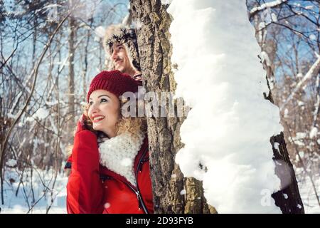 Verspieltes Paar versteckt sich hinter einen Baum im Schnee Stockfoto
