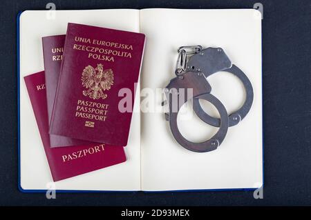 Handschellen, Reisepass und Notizbuch auf dem Tisch. Zubehör auf dem Schreibtisch auf der Polizeistation. Dunkler Hintergrund. Stockfoto