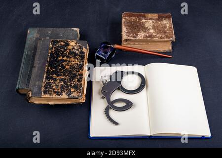 Handschellen und ein Notizbuch auf dem Tisch. Zubehör auf dem Schreibtisch der Polizeistation. Dunkler Hintergrund. Stockfoto