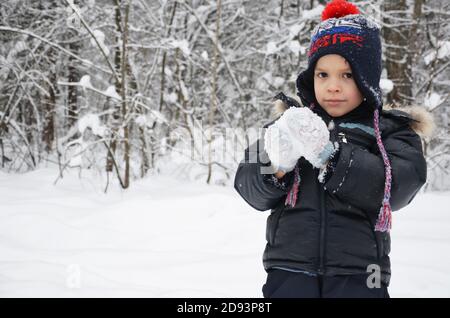 Ein schlichtes kleines Kind wirft Schnee im Winter schneebedeckten Wald, Bäume im Schnee. Genießt den Winter. Spielt Schneebälle. Glücklich, lächelnd, lacht Stockfoto