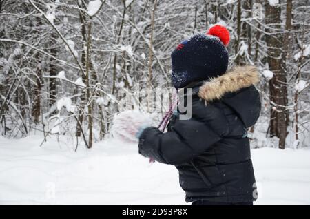 Ein schlichtes kleines Kind wirft Schnee im Winter schneebedeckten Wald, Bäume im Schnee. Genießt den Winter. Spielt Schneebälle. Glücklich, lächelnd, lacht Stockfoto