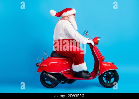 In voller Länge Profil Seite Foto von Fett weihnachtsmann mit Big Bart Laufwerk Roller Weihnachten weihnachten Neujahr tragen stilvolle moderne Hosenträger Overalls Hut Stockfoto