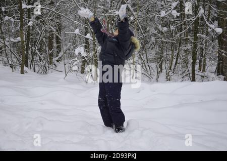 Ein schlichtes kleines Kind wirft Schnee im Winter schneebedeckten Wald, Bäume im Schnee. Genießt den Winter. Spielt Schneebälle. Glücklich, lächelnd, lacht Stockfoto