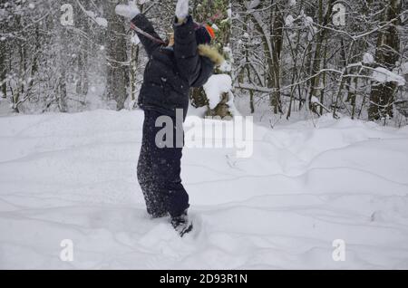 Ein schlichtes kleines Kind wirft Schnee im Winter schneebedeckten Wald, Bäume im Schnee. Genießt den Winter. Spielt Schneebälle. Glücklich, lächelnd, lacht Stockfoto