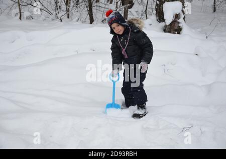 Ein schlichtes kleines Kind wirft Schnee im Winter schneebedeckten Wald, Bäume im Schnee. Genießt den Winter. Spielt Schneebälle. Glücklich, lächelnd, lacht Stockfoto