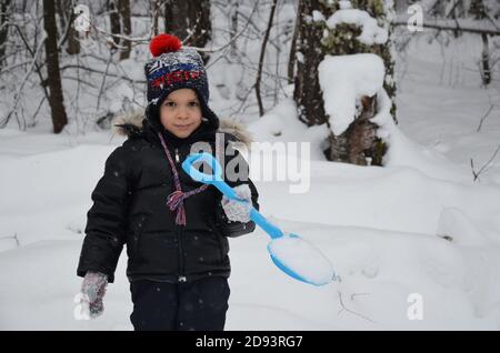 Ein schlichtes kleines Kind wirft Schnee im Winter schneebedeckten Wald, Bäume im Schnee. Genießt den Winter. Spielt Schneebälle. Glücklich, lächelnd, lacht Stockfoto