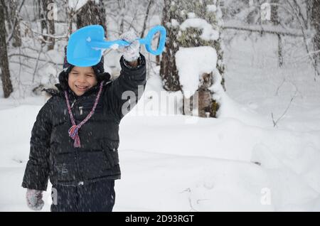 Ein schlichtes kleines Kind wirft Schnee im Winter schneebedeckten Wald, Bäume im Schnee. Genießt den Winter. Spielt Schneebälle. Glücklich, lächelnd, lacht Stockfoto