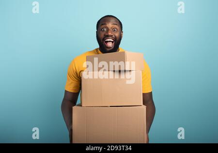 Glücklicher Mann hält eine Menge empfangene Pakete. Cyanfarbener Hintergrund Stockfoto