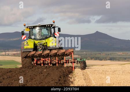 Ein Stoppelfeld, das mit einem Reversible Pflug gepflügt wird, der von einem Claas-Traktor gezogen wird, wobei Bennachie in Aberdeenshire am Horizont sichtbar ist Stockfoto