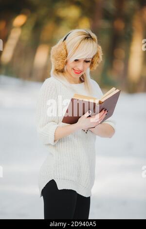 Schöne blonde Mädchen in einem weißen Pullover mit hellen Make-up im Winter ein Buch im Park zu lesen. Stockfoto