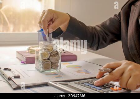 Ein Geschäftsmann hält eine Münze in einem Sparschwein und drücken Sie einen Rechner Finanzkonzept und Finanzbuchhaltung. Stockfoto