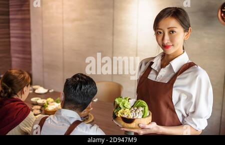 Der Kellner brachte Gemüse für den heißen Topf und servierte Gäste Restaurant Stockfoto