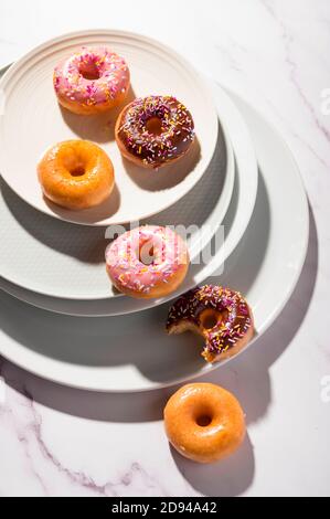 Donuts mit verschiedenen Glasuren, traditionelle süße Backwaren mit Streuseln auf weißem Marmor Hintergrund gekrönt Stockfoto
