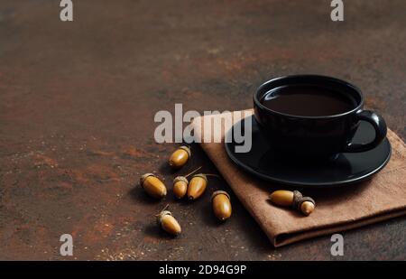 Kaffee in einer schwarzen Tasse und Eicheln auf braunem Hintergrund. Acorn Kaffee ohne Koffein. Leerzeichen für Text. Seitenansicht. Stockfoto
