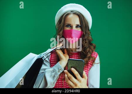 Leben während einer Coronavirus-Pandemie. Portrait von glücklich moderne weibliche Shopper in rosa ärmellose Hemd mit rosa medizinische Maske und Einkaufstaschen Kauf onl Stockfoto