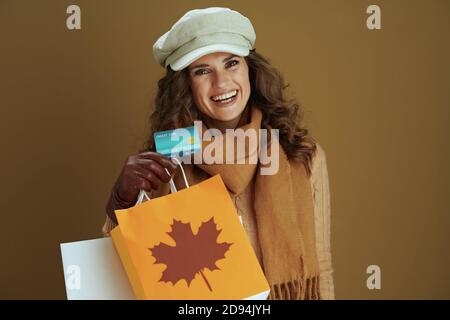 Hallo november. Portrait der lächelnden eleganten Hausfrau im Schal mit Lederhandschuhen und Papier Einkaufstasche auf braunem Hintergrund. Stockfoto