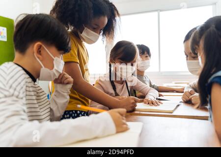 Junge Lehrerin, die ein Alkoholspray verwendet, um die Hände der Schüler im Klassenzimmer zu desinfizieren. Asiatische Frau in Gesichtsmaske Reinigung Pupillen Hände mit Hand Desinfektionsmittel. Schule nach Quarantäne und Sperrung wieder öffnen. Stockfoto