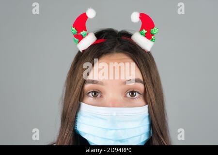 Eine junge Frau in einer medizinischen Maske mit Weihnachtsdekoration auf dem Kopf. Grauer Hintergrund. Hochwertige Fotos Stockfoto