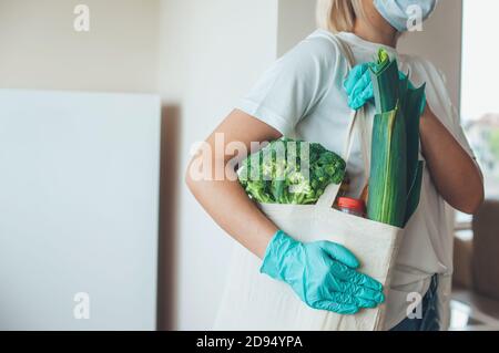 Blonde Frau mit Handschuhen und Maske liefert Nahrung Ein Beutel während der Pandemie-Zeit Stockfoto