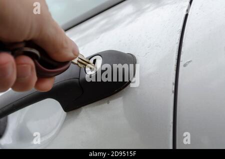 Die Hand des Mannes führt den Schlüssel in das Türschloss des Autos ein. Der Mann öffnet das Auto. Nahaufnahme. Selektiver Fokus. Stockfoto