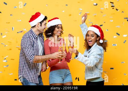 Eine Gruppe verschiedener Freunde trinkt Champagner und feiert Weihnachten auf Gelb Farbe Studio Hintergrund mit Konfetti Stockfoto