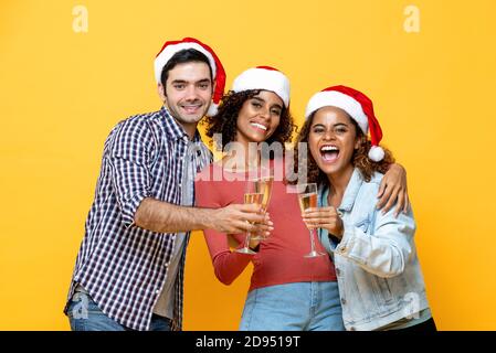 Eine Gruppe von drei begeisterten verschiedenen Freunden feiern Weihnachten trinken Champagner Zusammen auf gelbem Studiohintergrund Stockfoto