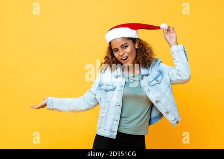 Fun Taille bis Porträt von fröhlichen afroamerikanischen Frau tragen Weihnachtsmütze mit offener Palmgeste auf gelbem isoliertem Hintergrund Stockfoto