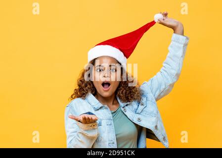 Lustig überrascht afroamerikanische Frau trägt Weihnachtshut mit offen Handbewegung auf gelbem, isoliertem Hintergrund Stockfoto