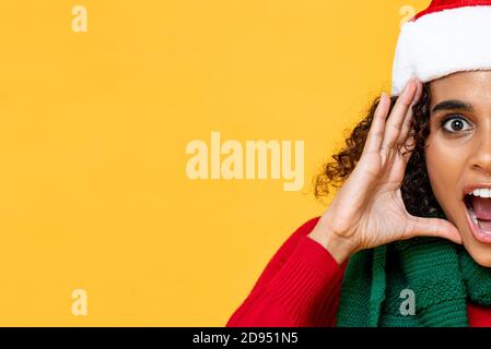 Das halbe Gesicht einer schockierten Frau in Weihnachtskleidung, die einbrüllt Gelber isolierter Studiohintergrund mit Kopierbereich Stockfoto
