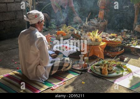 Rückansicht des hinduistischen Priesters, der während einer Hochzeitszeremonie betet. Pedanda sitzt auf dem Boden vor den Opfergaben und führt Hochzeitszeremonien durch Stockfoto
