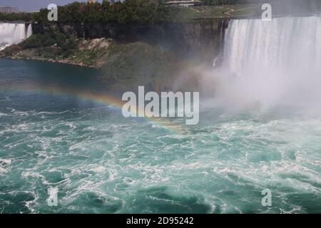 Ein Blick auf die Niagarafälle mit einem Regenbogen am Boden gebildet. Sie können den Nebel sehen, der sich aus dem Wasser gebildet hat, das auf die Felsen darunter trifft Stockfoto