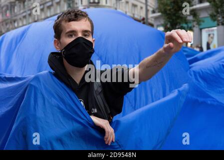 Während der Demonstration ist ein Aktivist mit Gesichtsmaske im blauen Tuch zu sehen.während der dritten internationalen Rebellion blockierte die Bewegung Extinction Rebellion die Gran Vía Straße in Madrid, um gegen die Folgen des steigenden Meeresspiegels zu protestieren. Die Bewegung, die ein 150 Quadratmeter blaues Tuch vom Callao-Platz zum spanischen Platz trägt, marschiert über die Gran Vía-Straße, um die wachsende Zahl der Menschen sichtbar zu machen, die vom Anstieg des Meeresspiegels, verursacht durch den Klimawandel, betroffen sind. Dieser Akt unter dem Namen "Wir sinken" hat die große Zahl der Todesfälle durch den Anstieg des Meeresspiegels dargestellt. Stockfoto