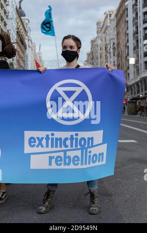 Ein Aktivist mit Gesichtsmaske hält während der Demonstration ein Banner mit dem Logo der Extinction Rebellion.während der dritten internationalen Rebellion blockierte die Extinction Rebellion Bewegung die Gran Vía Straße in Madrid, um gegen die Folgen des steigenden Meeresspiegels zu protestieren. Die Bewegung, die ein 150 Quadratmeter blaues Tuch vom Callao-Platz zum spanischen Platz trägt, marschiert über die Gran Vía-Straße, um die wachsende Zahl der Menschen sichtbar zu machen, die vom Anstieg des Meeresspiegels, verursacht durch den Klimawandel, betroffen sind. Dieser Akt unter dem Namen "Wir sinken" hat die große Zahl der Todesfälle durch den Anstieg der See dargestellt Stockfoto