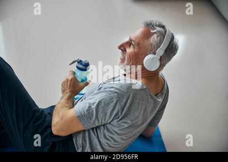 Aktiver älterer Mann mit Kopfhörern lächelt während er sich vom Training ausruhte Stockfoto